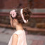 Young girl in a pink dress with floral hair accessories sitting on a stone bench.