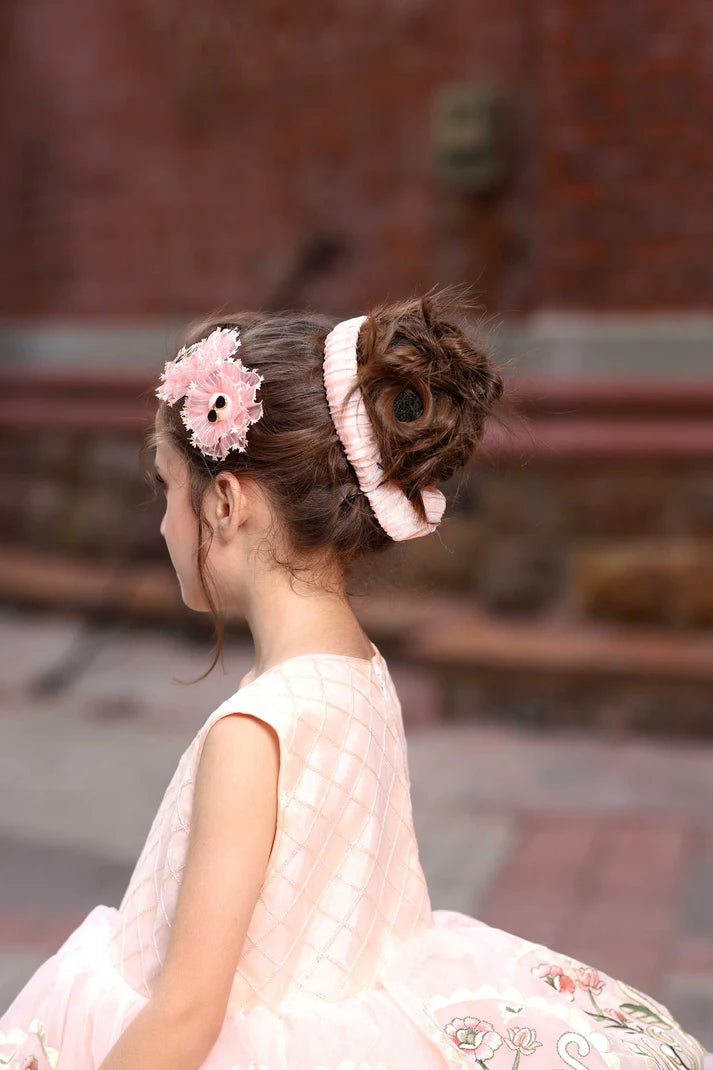 Young girl in a pink dress with floral hair accessories sitting on a stone bench.