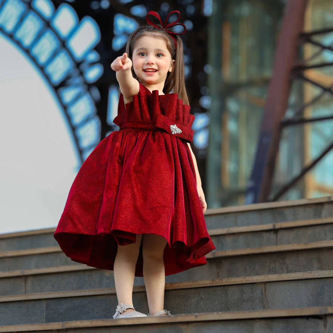 Young girl in a red dress standing on steps with a decorative background