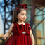 Young girl in a red dress with a large bow in her hair, standing outdoors.