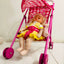 Toy doll in a pink stroller with a checkered pattern on a light background