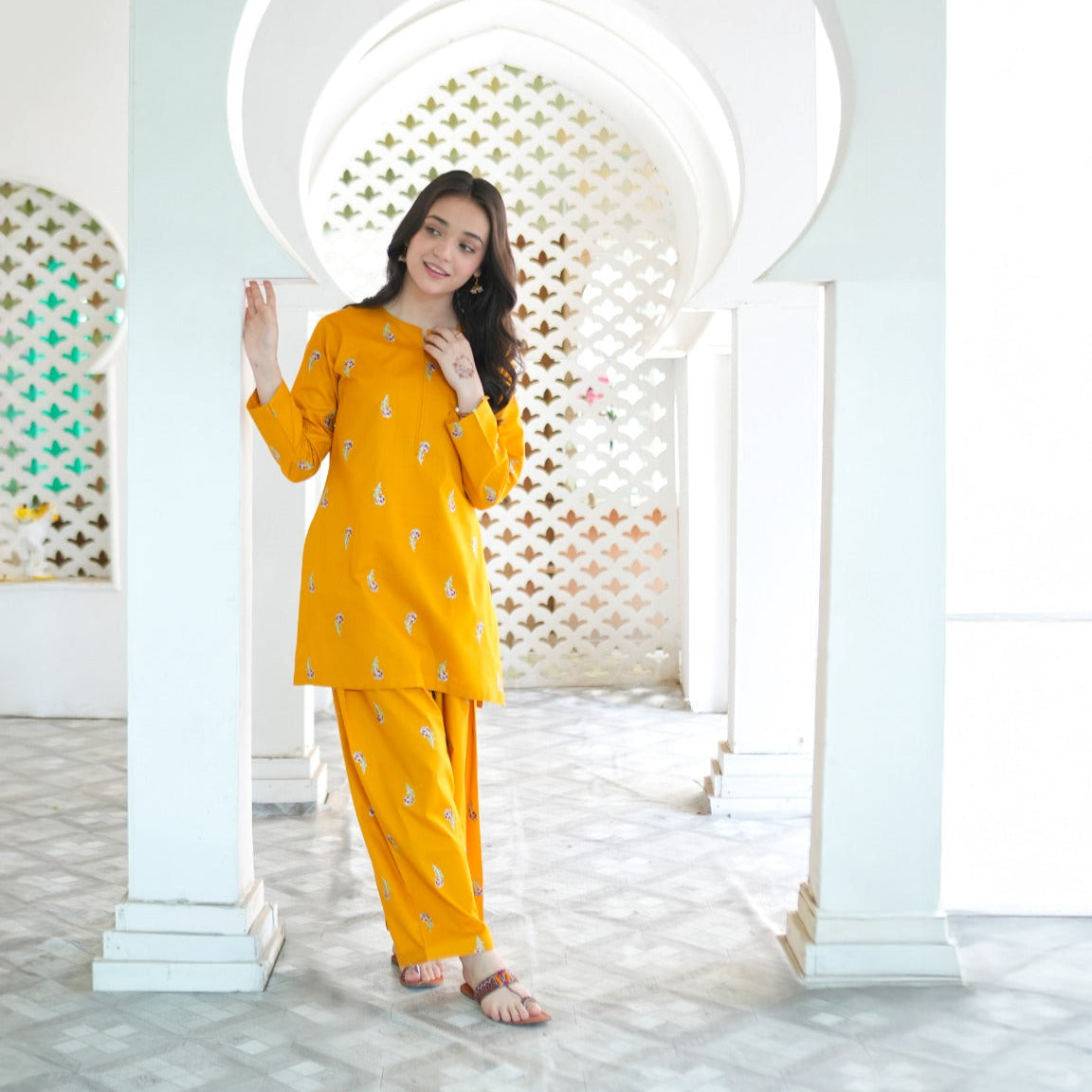 Woman in a yellow traditional outfit standing in front of an archway.