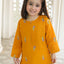 Young girl wearing a yellow outfit with floral patterns indoors.