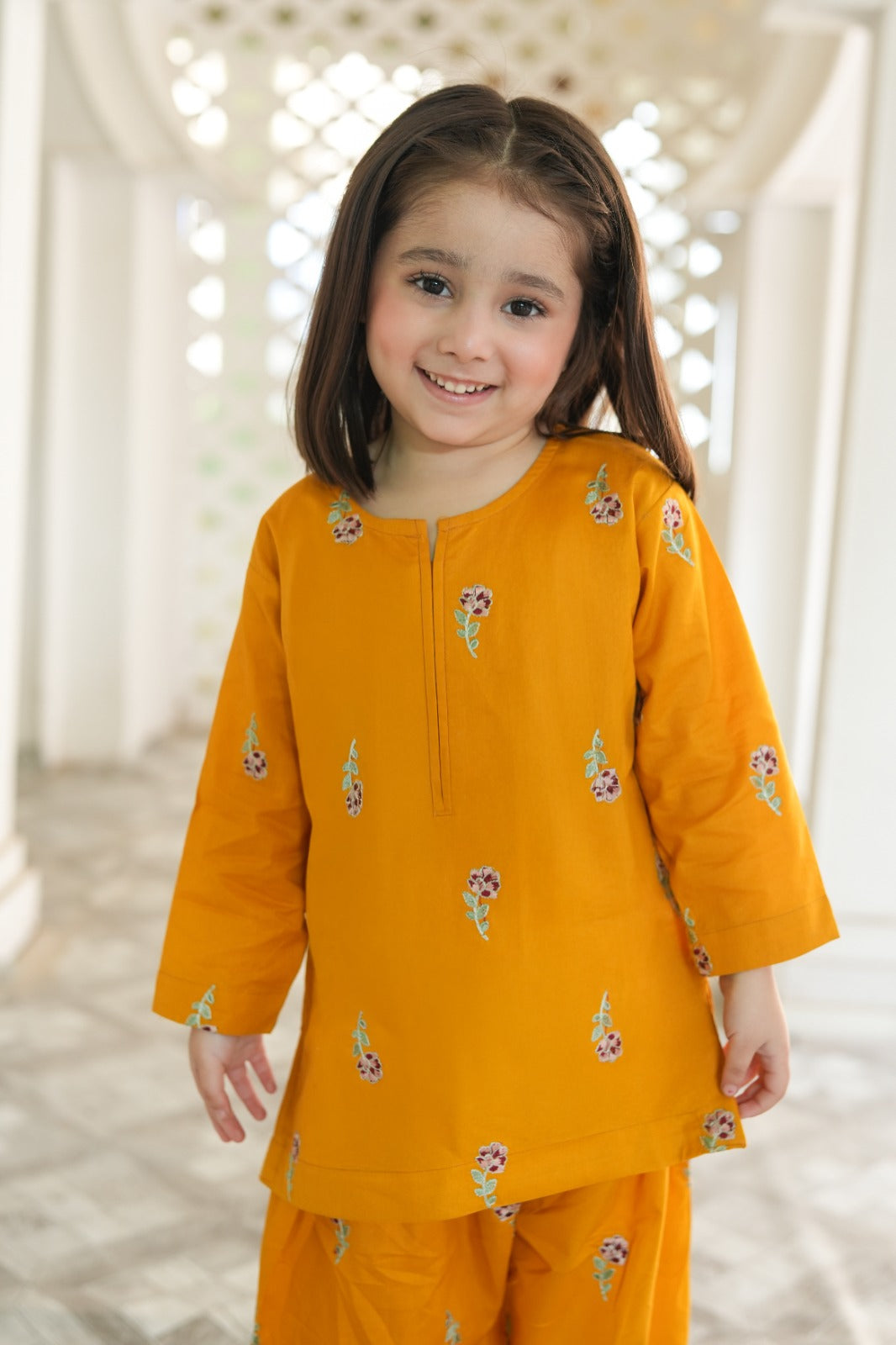 Young girl wearing a yellow outfit with floral patterns indoors.