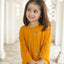 Young girl wearing a mustard yellow traditional outfit with floral patterns indoors.
