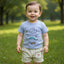 Child wearing a light blue t-shirt with dinosaur designs and striped shorts.