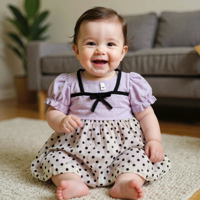 Baby in a polka dot outfit sitting on a carpeted floor 