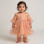 Child wearing a peach-colored dress with floral embroidery