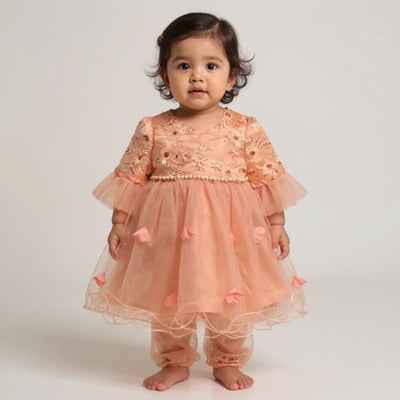 Child wearing a peach-colored dress with floral embroidery